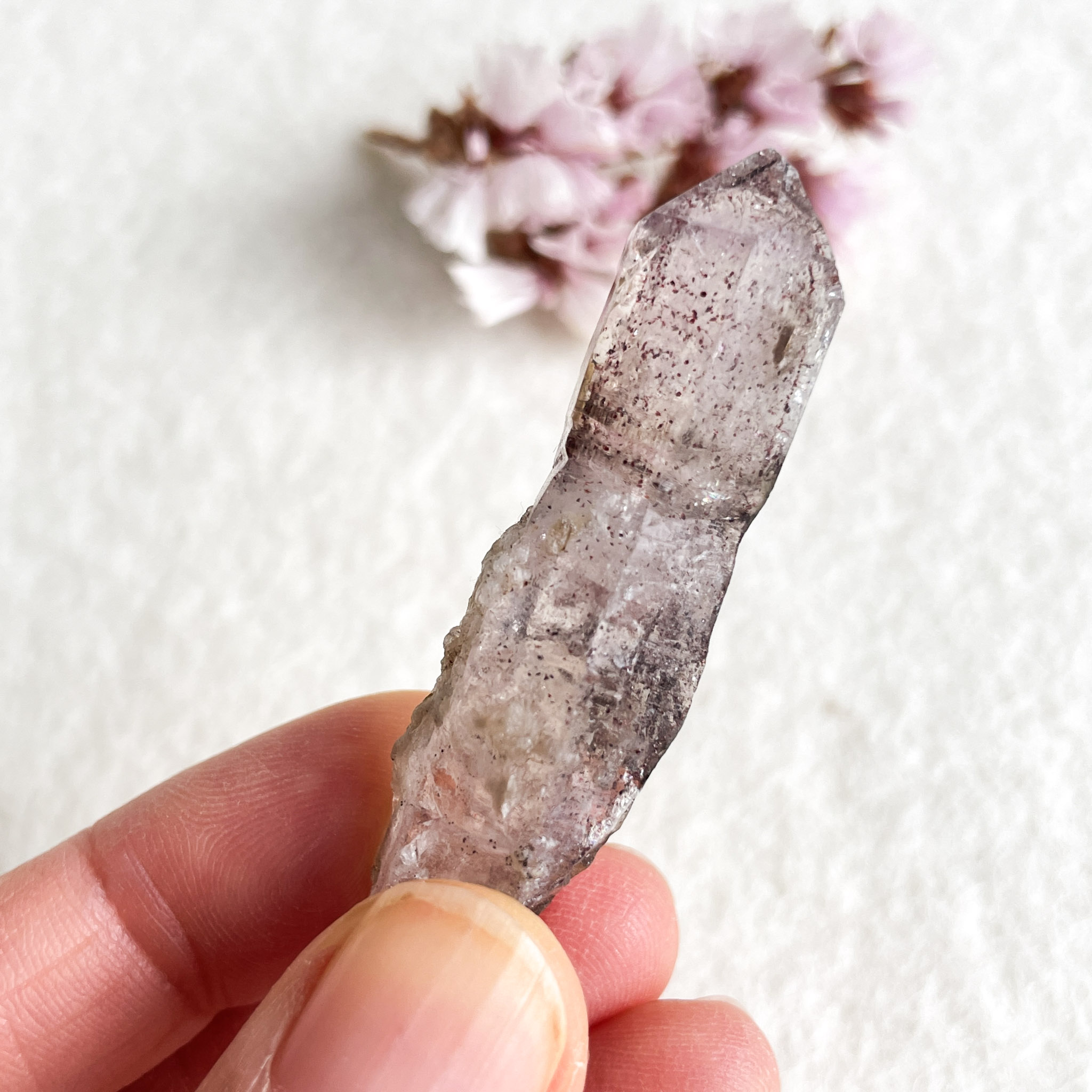 A close-up photo of a hand holding a quartz crystal, with a blurred blossom in the background.
