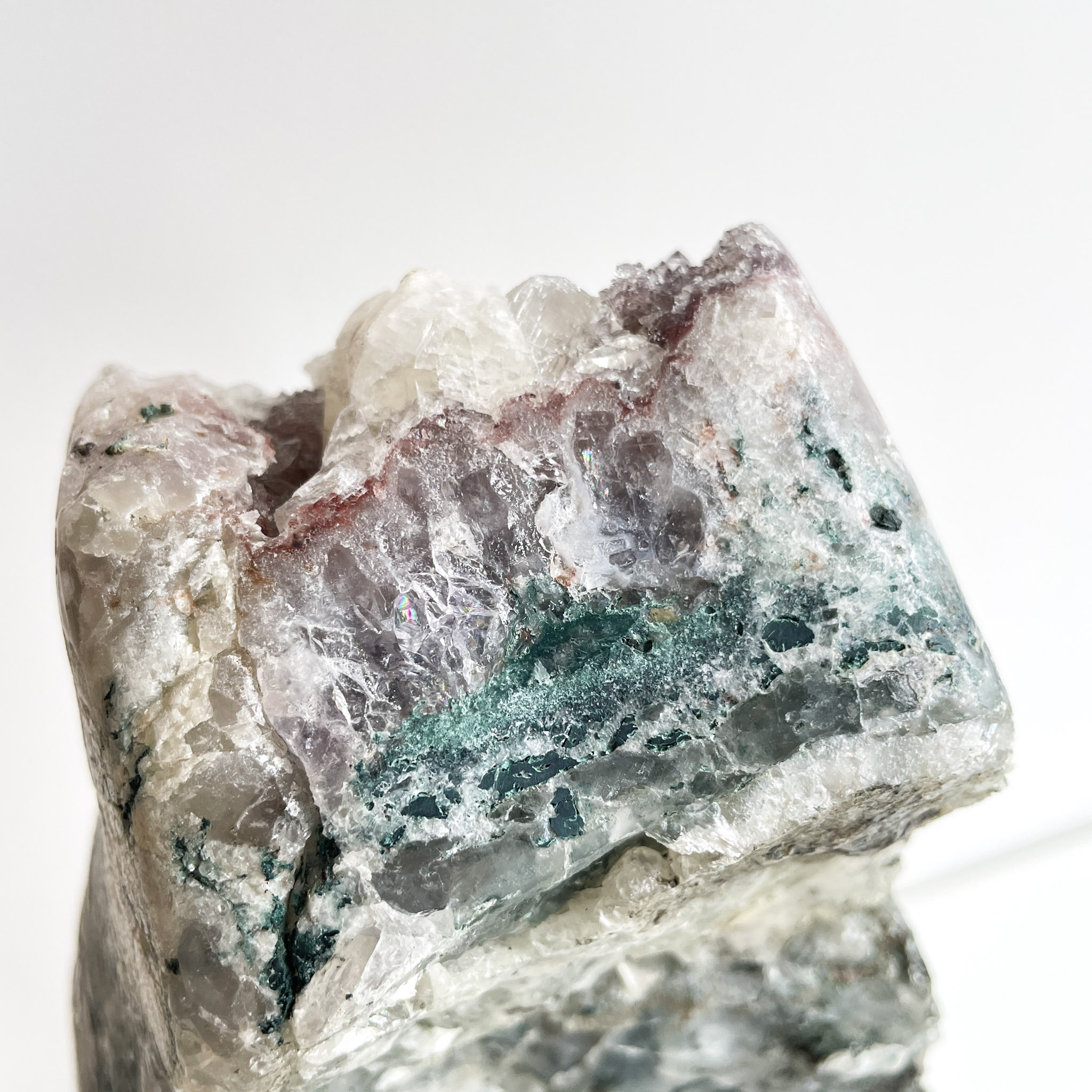 A close-up image of a rough mineral specimen with various translucent and opaque crystalline structures in shades of white, purple, and green.
