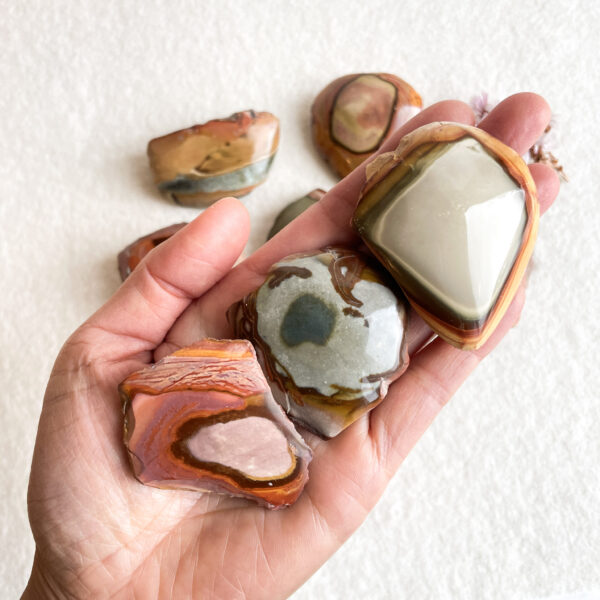 A person's hand holding several polished stones with various colors and patterns.