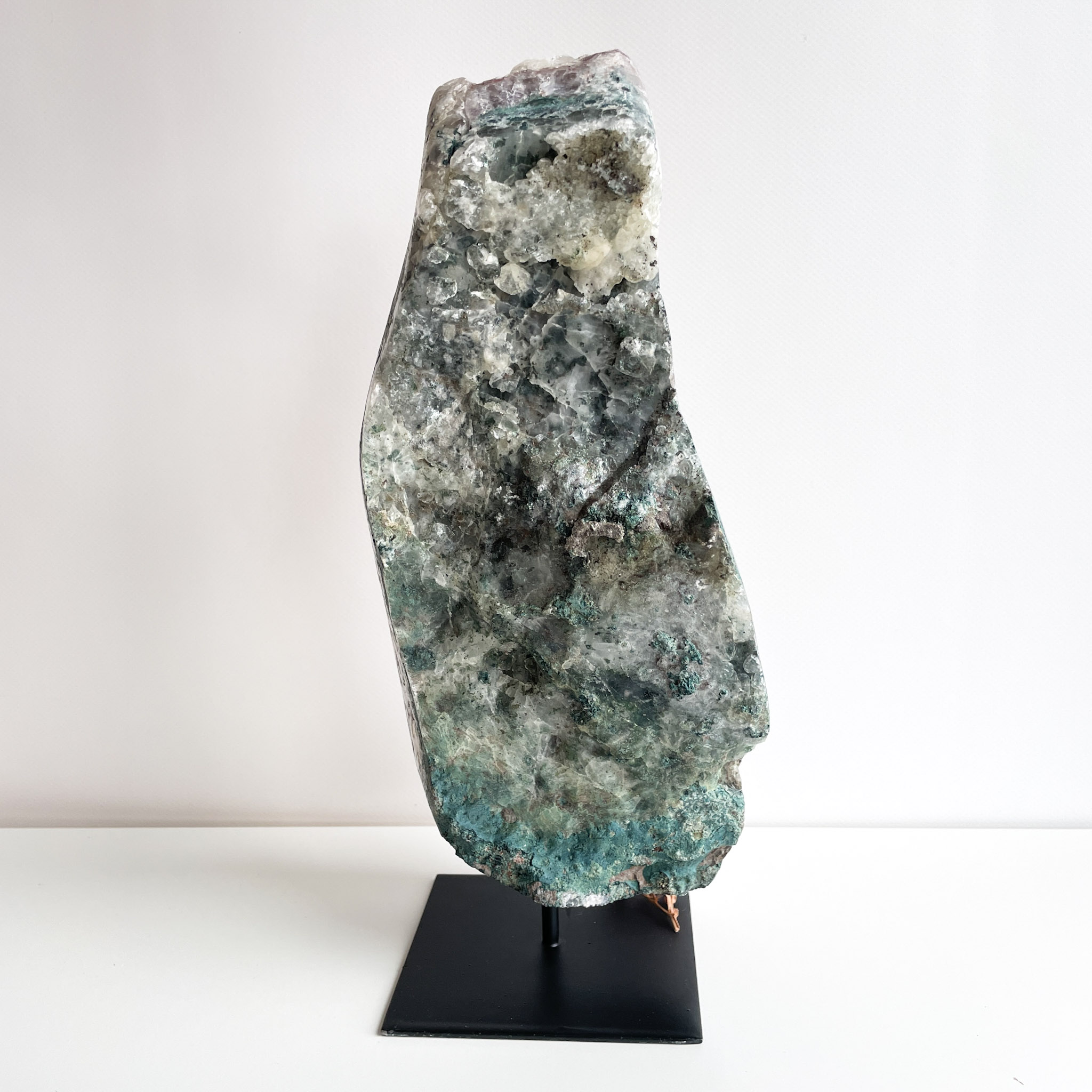 A large, multicolored mineral specimen mounted upright on a black display stand with a white background.