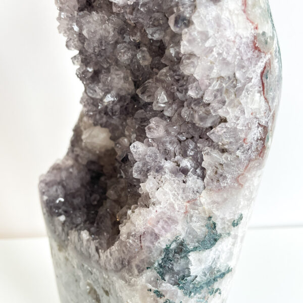 Close-up of a geode with various shades of purple and white crystals against a white background.