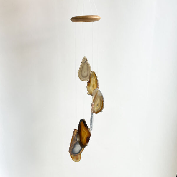 A mobile hanging from the ceiling featuring several slices of agate stones in various earth tones, suspended by thin threads from a round wooden top.
