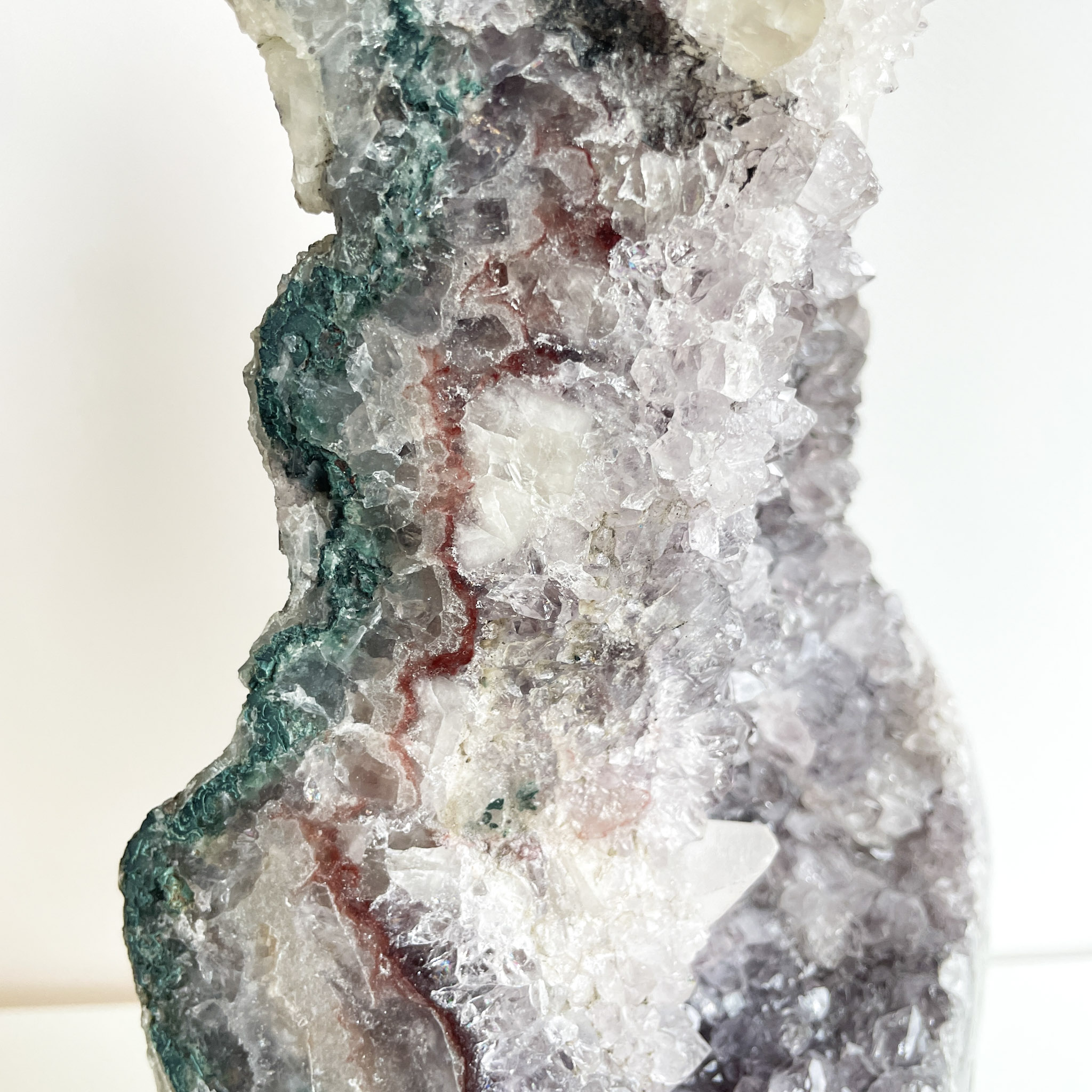 Close-up of a multi-colored geode with crystalline structures, featuring shades of white, green, and patches of red.