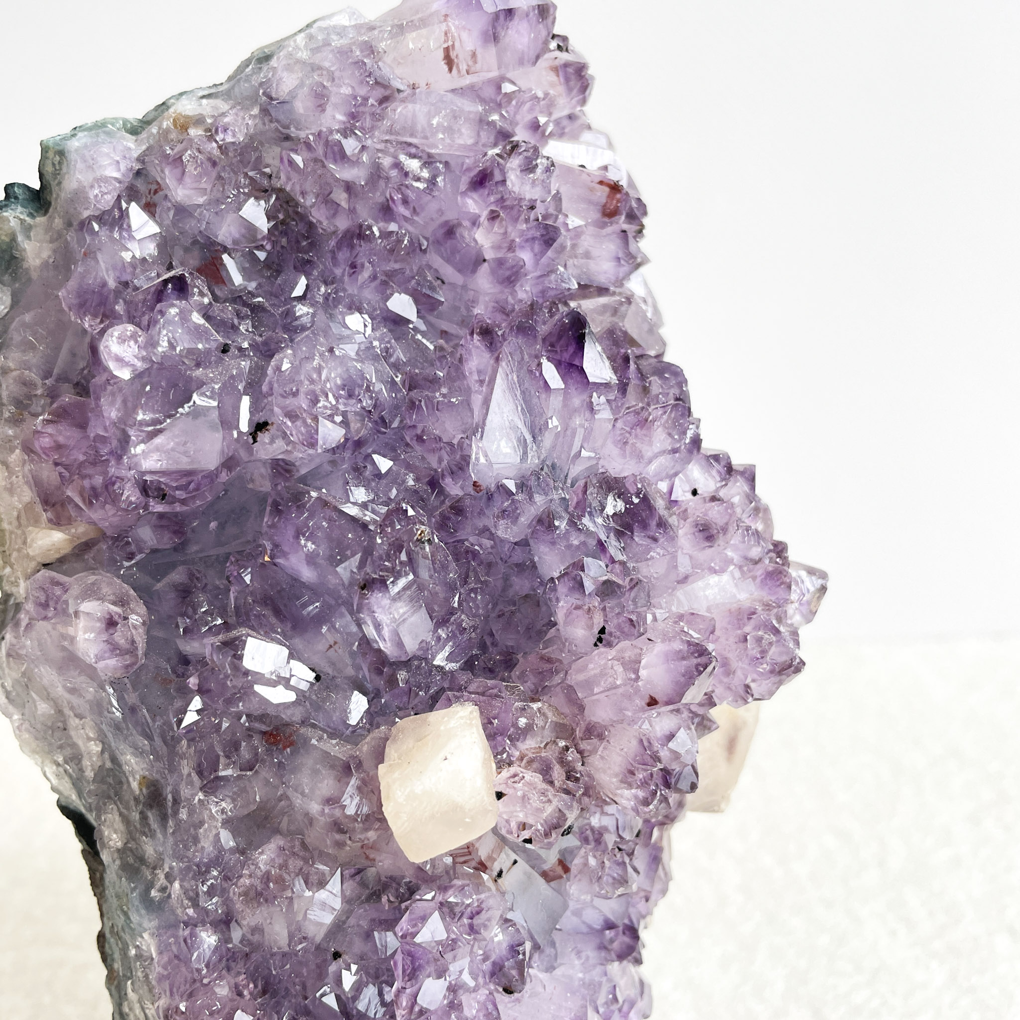 A close-up of a purple amethyst geode with sparkling crystal points on a light background.