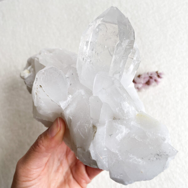 A person holding a large clear quartz crystal cluster against a white textured background.