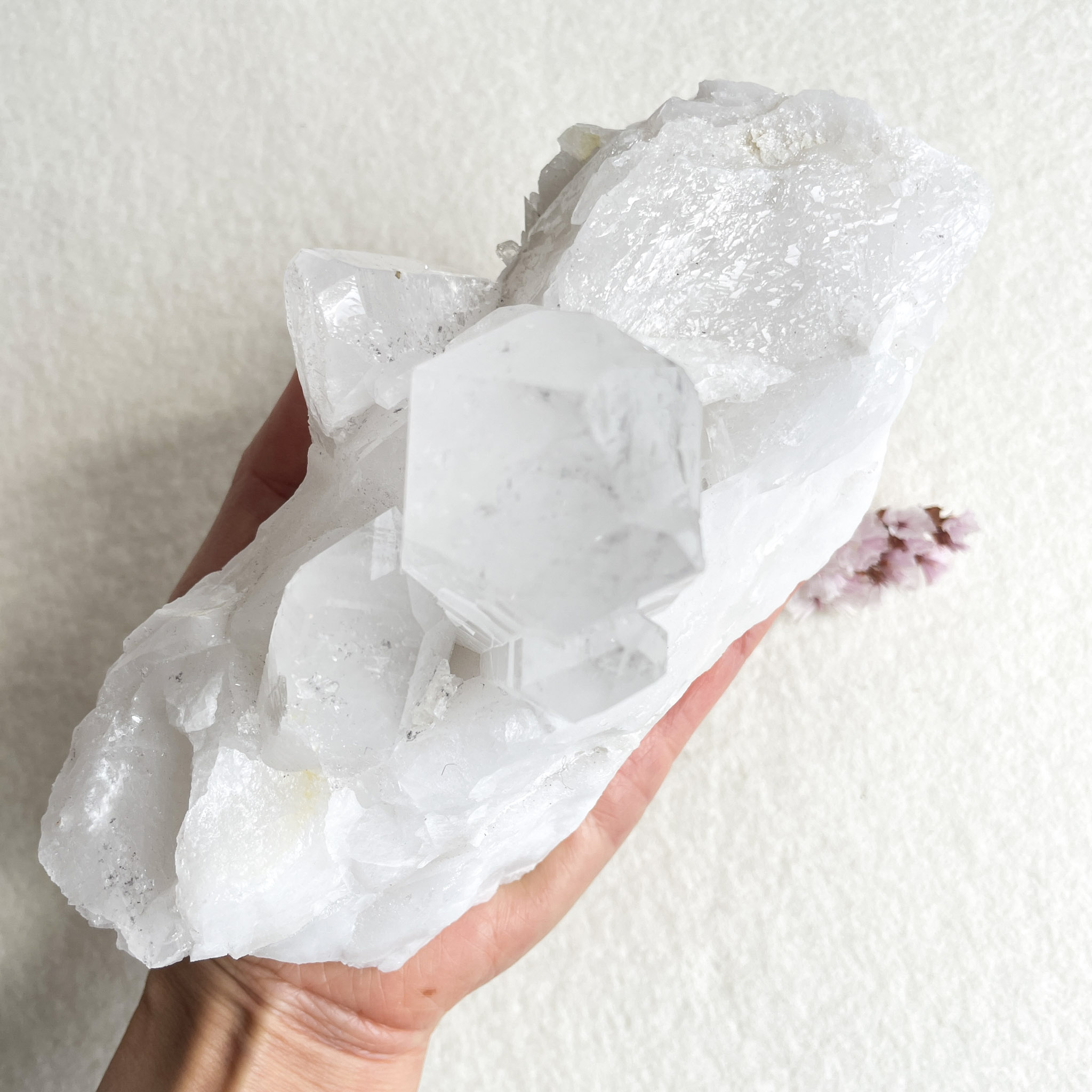 A person holding a large, clear crystal with multiple facets and edges in the palm of their hand.