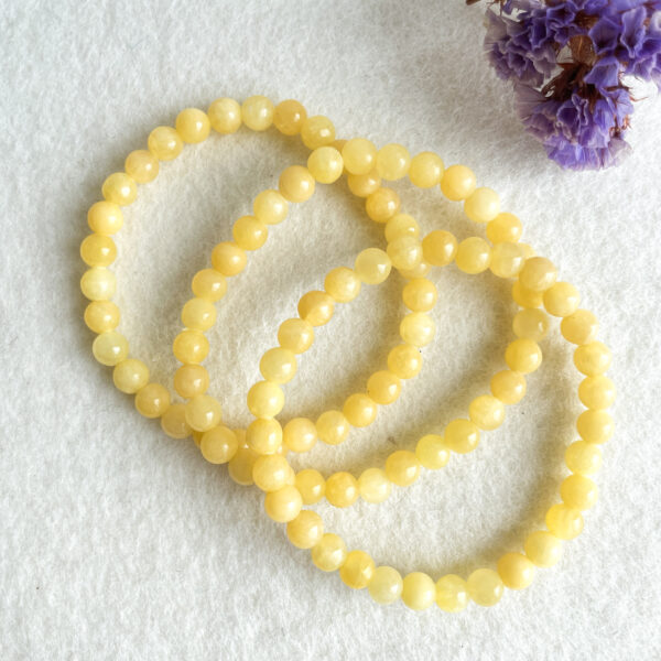 Three strands of yellow beads on a white surface with a blurred purple flower in the corner.
