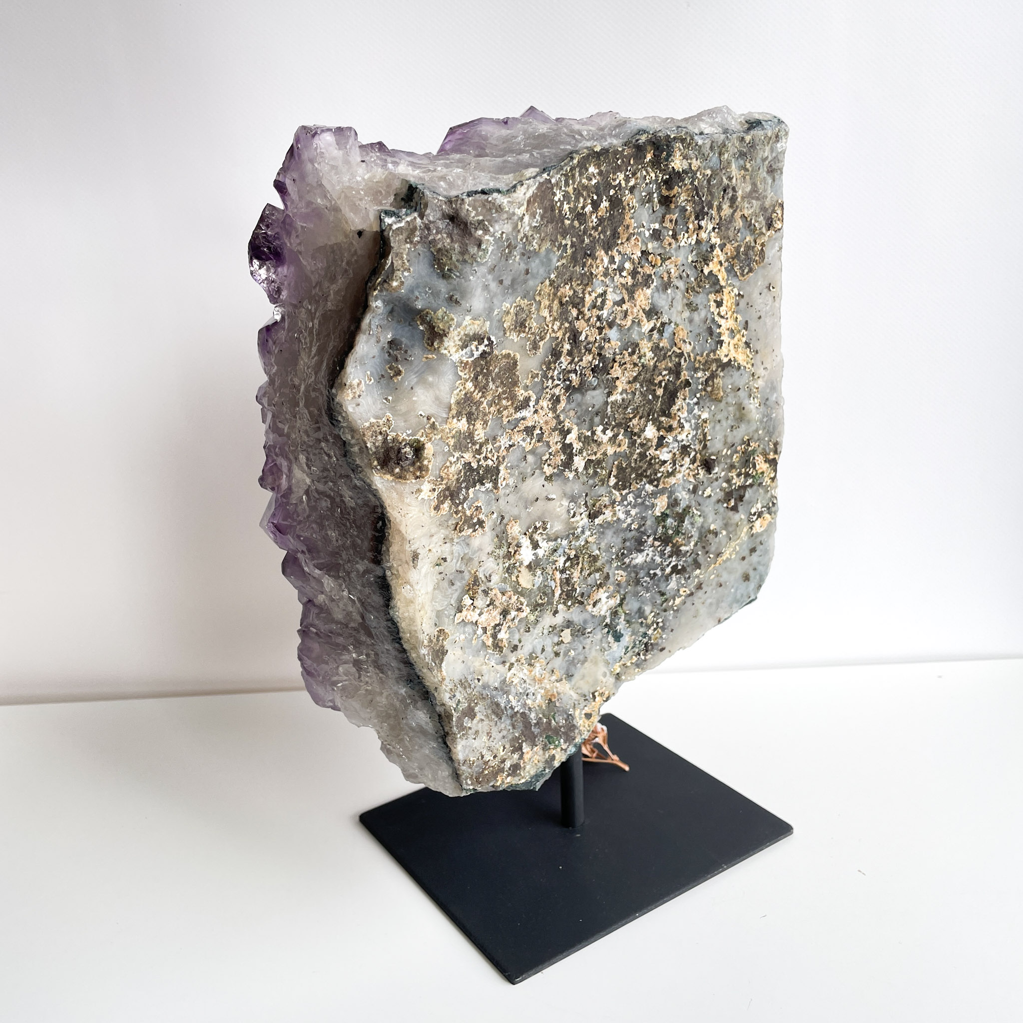 A large amethyst geode on a black stand with visible quartz crystals framing the purple amethyst interior, against a white background.