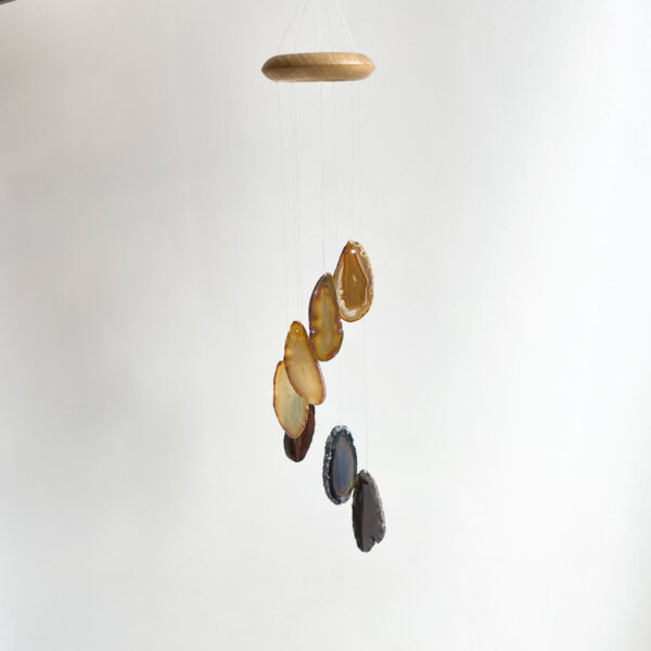 A mobile hanging with sliced agate stones in various brown and blue hues suspended from a wooden ring against a white background.