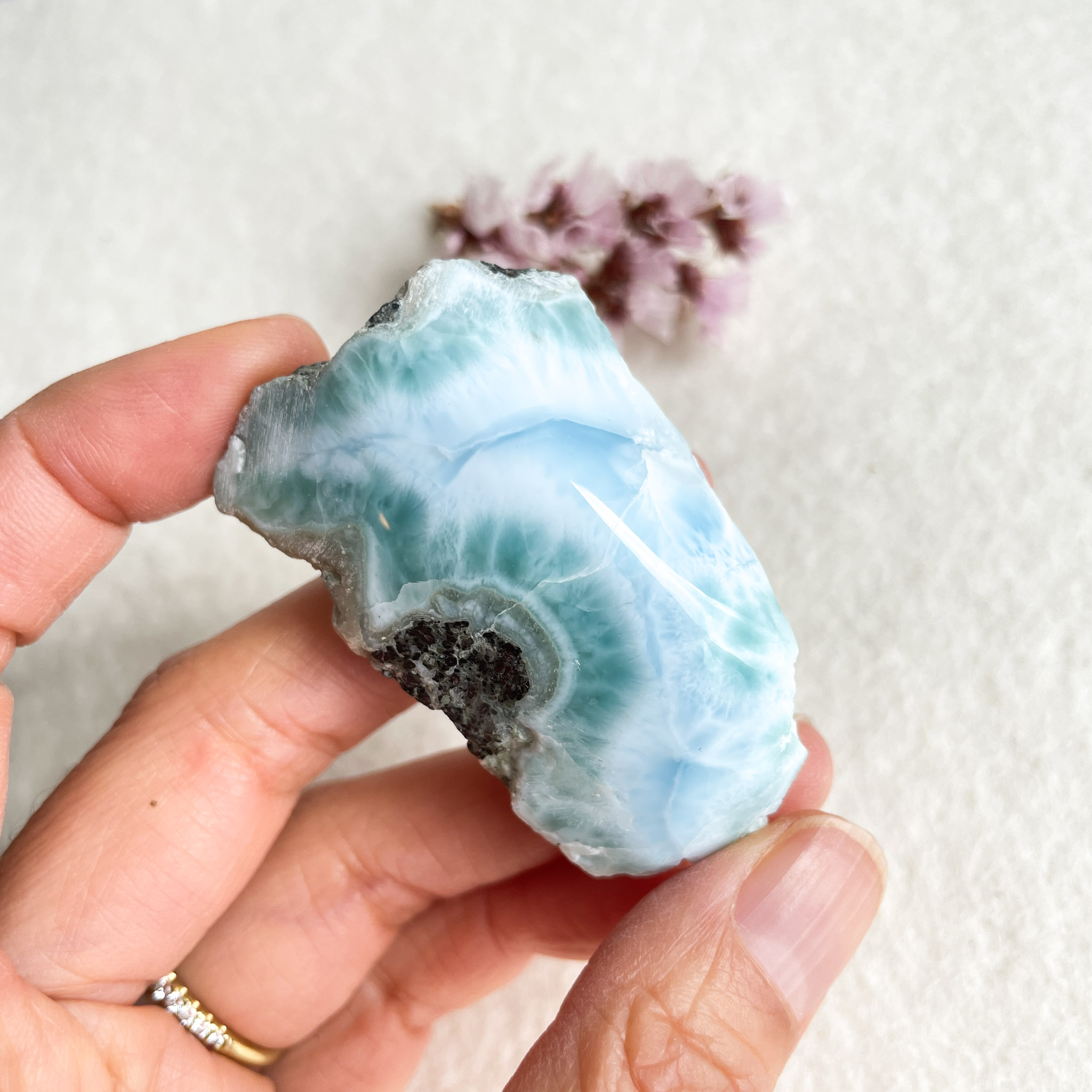 A person holds a polished blue and white agate stone with a crystalline center and rough edges, with small dried flowers in the background.