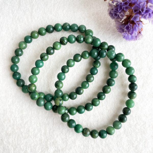 Three strands of green jade beads laid on a white surface, next to a purple dried flower.