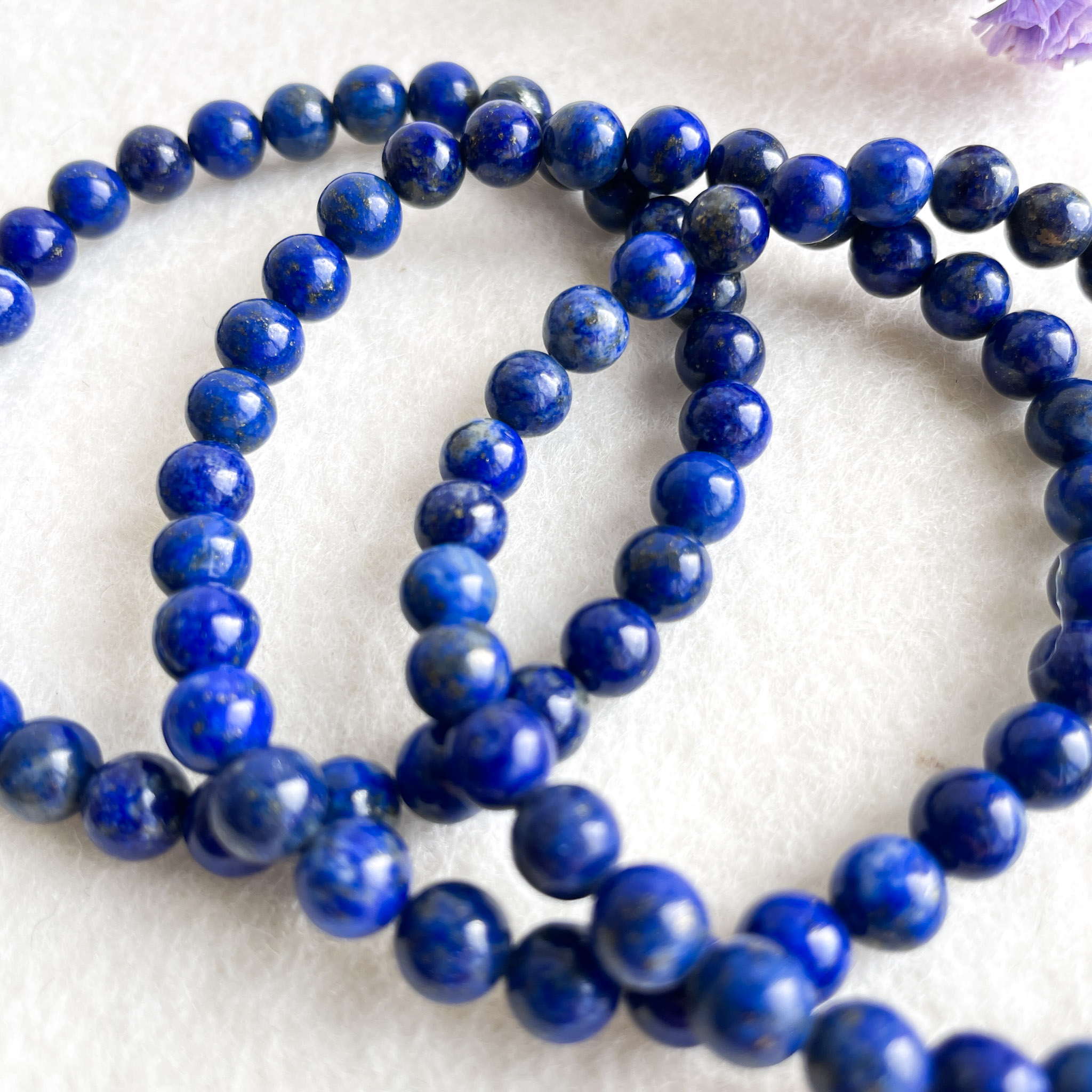 A string of lapis lazuli beads with a deep blue color and natural gold flecks, arranged in a loop on a white surface.