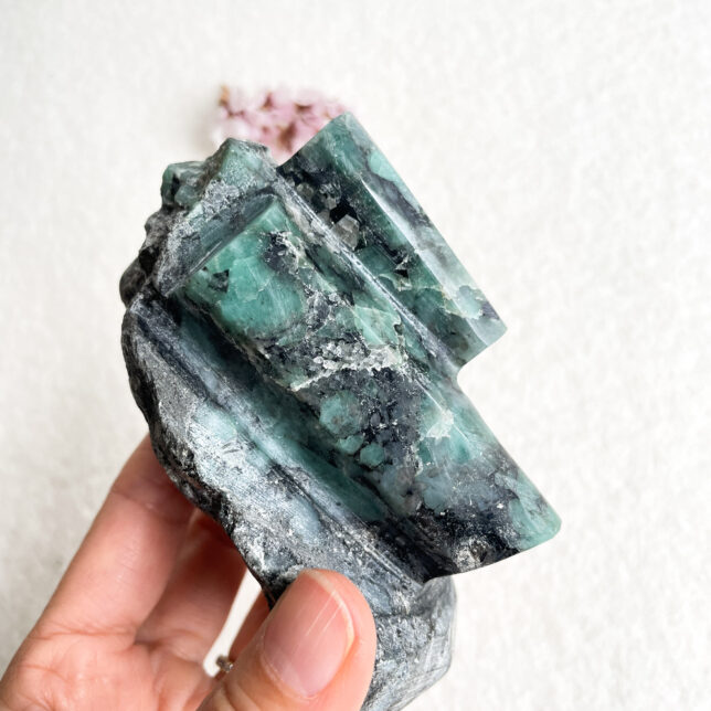 A person's hand holding a cluster of green fluorite crystals with prominent cubic structures against a textured white background.