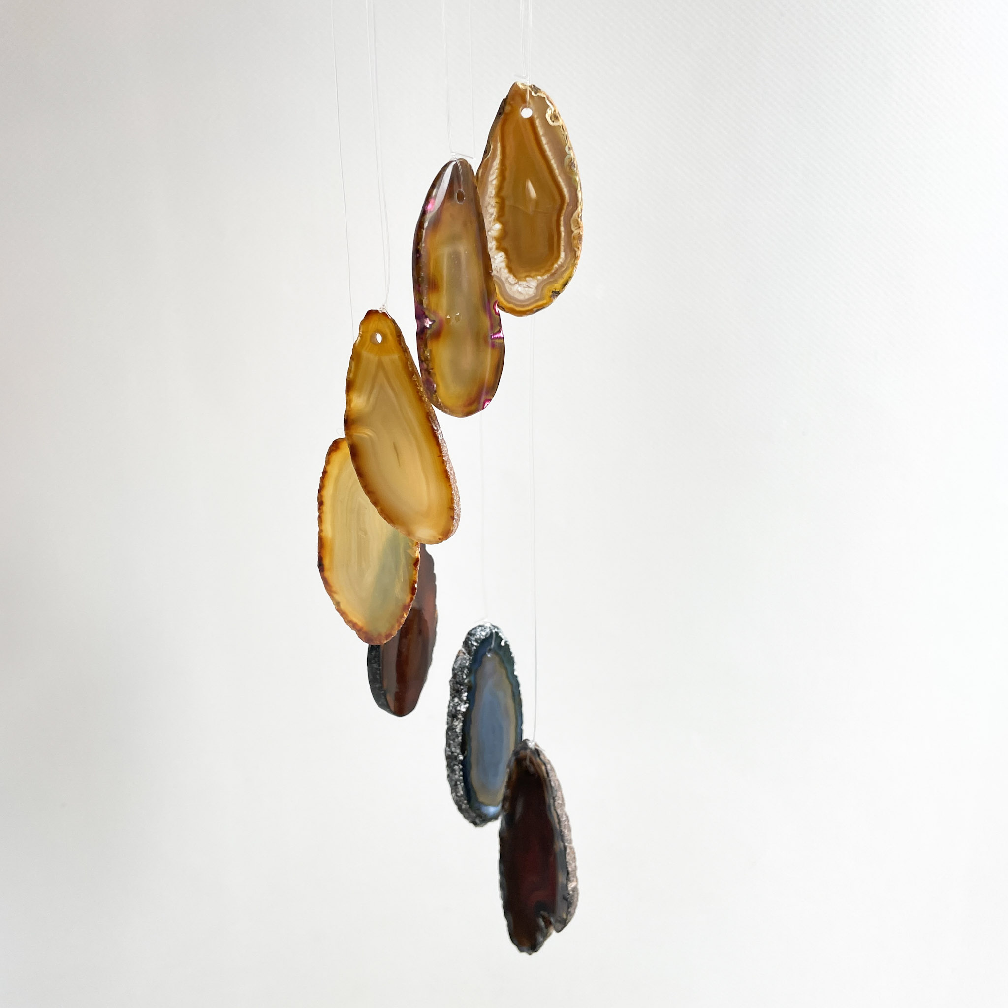 Sliced agate stones hanging by threads against a white background, showing varied colors and natural patterns.