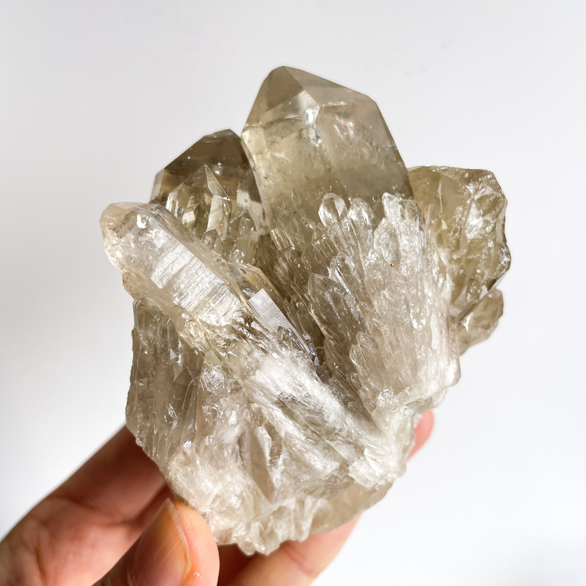 A hand holding a cluster of transparent quartz crystals against a white background.