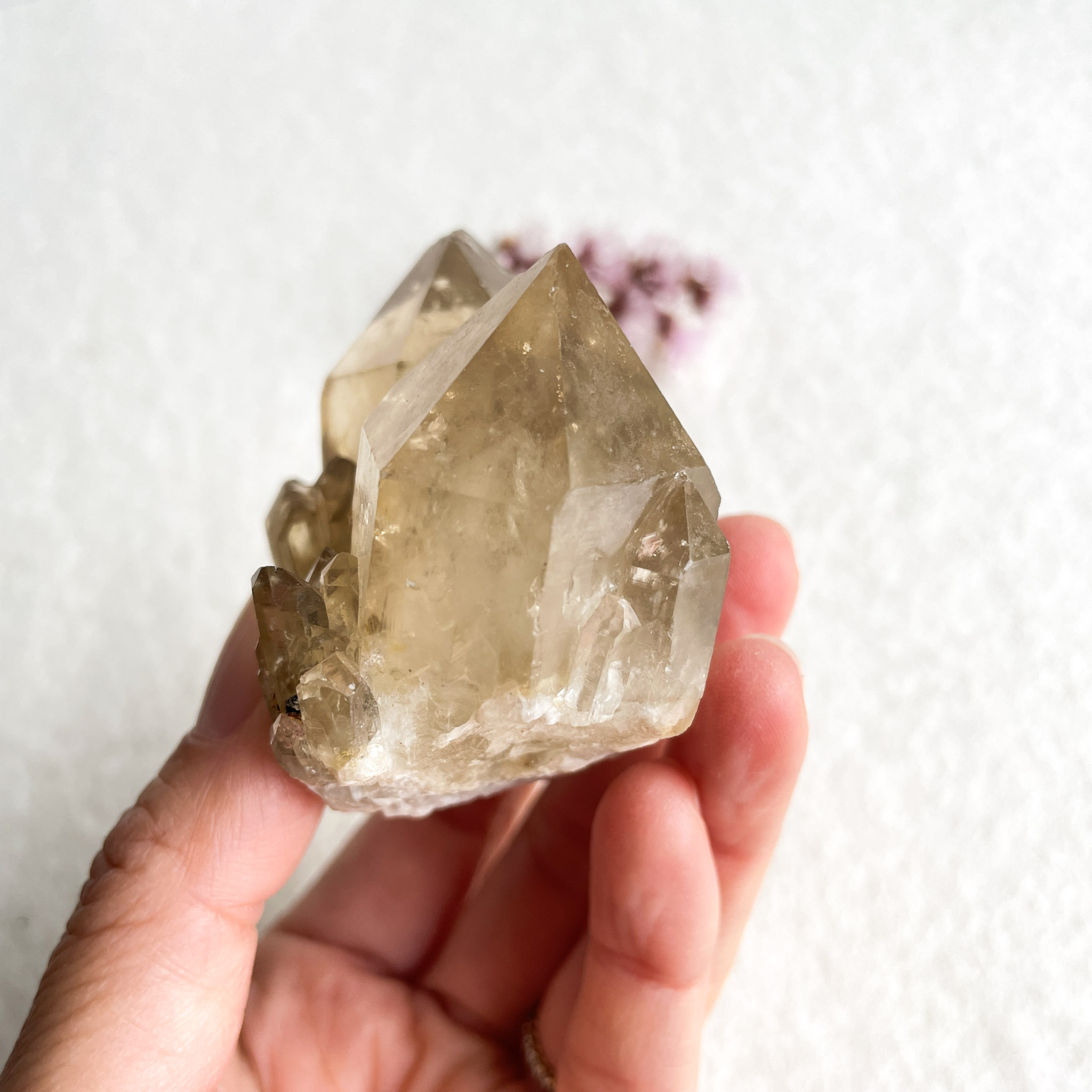 A person's hand holding a large, translucent crystal with multiple facets against a white background with a soft blurred element in the corner.