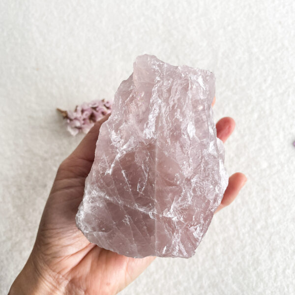 A person holding a large, rough pink quartz crystal in their hand with a blurred background.