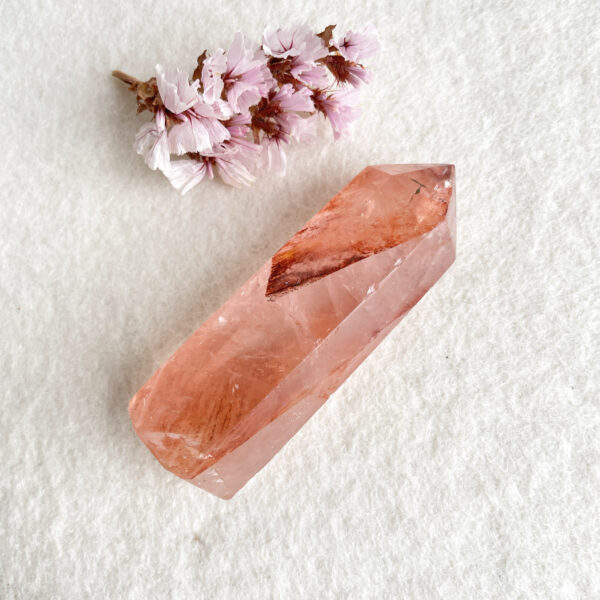 A translucent pink crystal on a white textured background, with a small cluster of cherry blossoms to the left.