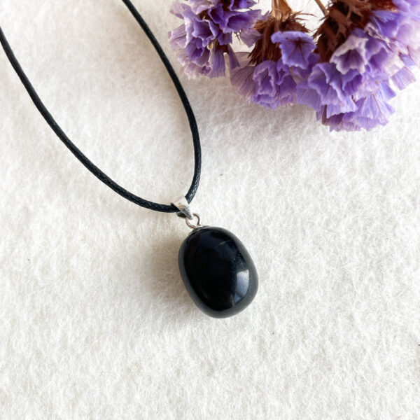 A black pendant on a leather cord next to purple dried flowers on a textured white background.